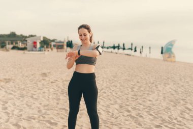 Fitness Tracker 'da kalp atışlarını kontrol eden genç bir kadın. Sabahın erken saatlerinde deniz kenarında koşarken.