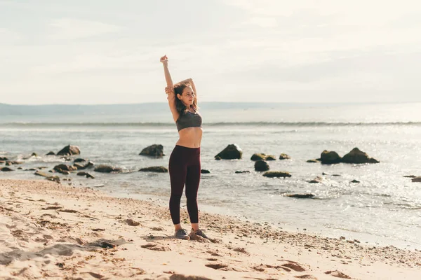 Женщина бегун делает упражнения на растяжку на пляже, утренний пробег, фитнес и здоровый образ жизни концепции — стоковое фото