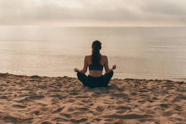Jóga nő reggel a tengerparton, egy lány jóga lótusz meditációs pozícióban elöl a tengerparton napkeltekor — Stock Fotó