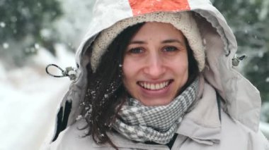 Ormanda dikilen ve kar yağan neşeli genç bir kadının görüntülerini kapatın.