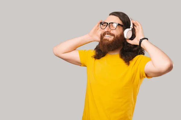Joyeux jeune homme barbu portant un t-shirt jaune écoutant de la musique sur des écouteurs sans fil blancs — Photo