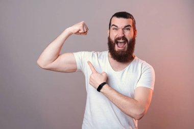 Şaşkın sakallı genç adam pazılarını gösteriyor.