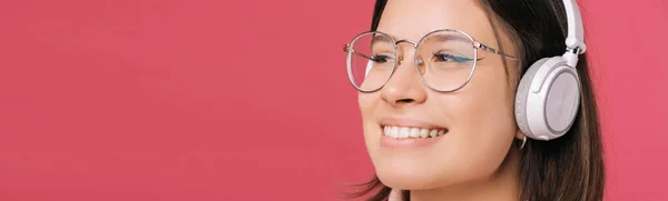 Foto ravvicinata di affascinante giovane donna che indossa occhiali e ascolta musica con cuffie wireless bianche — Foto Stock