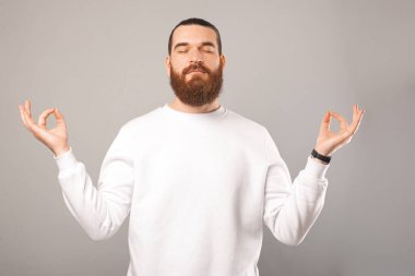 Pozitif sakallı adam ayakta duruyor ve zen jestiyle el ele tutuşuyor..