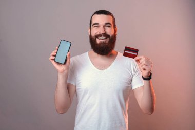 Neşeli sakallı adam telefonunu ve kredi kartını tutuyor..