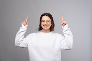 Geniş gülümseyen kadın iki eliyle gri arka planı işaret ediyor..