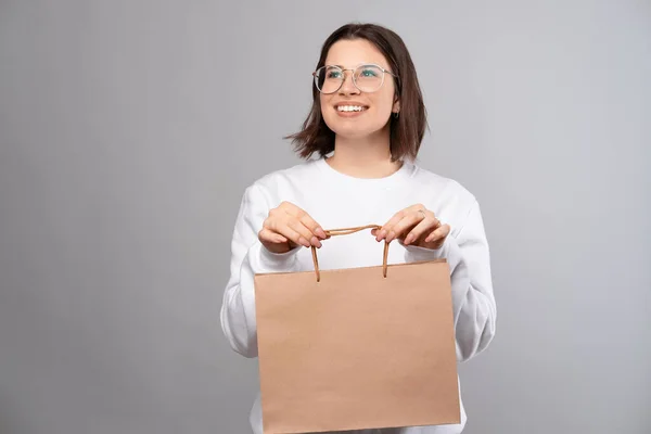 Улыбающаяся молодая женщина держит пакет с покупками и смотрит в сторону — стоковое фото