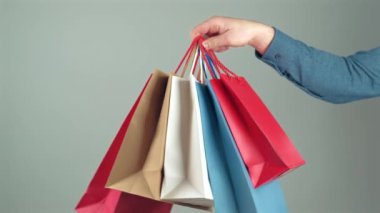 Gri arkaplanda bir sürü kağıt alışveriş torbası tutan bir adamın görüntüsü.