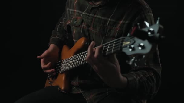 Filmaufnahme eines Mannes, der auf einer Bassgitarre mit 5 Saiten vor dunklem Hintergrund spielt — Stockvideo