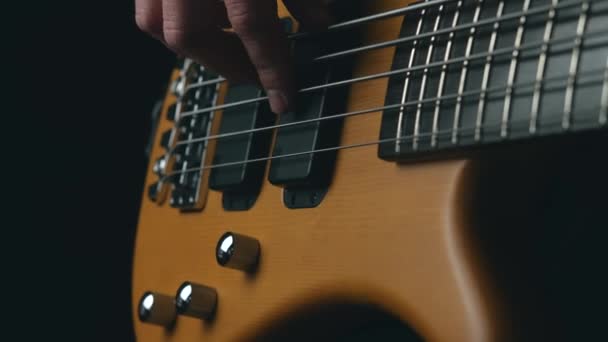 Nahaufnahme von Zeitlupenaufnahmen eines Mannes, der auf einer Bassgitarre vor dunklem Hintergrund spielt — Stockvideo