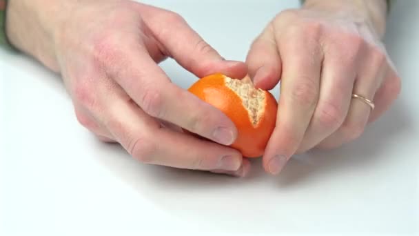 Imágenes de cerca del hombre pelando una naranja sobre una mesa blanca — Vídeos de Stock