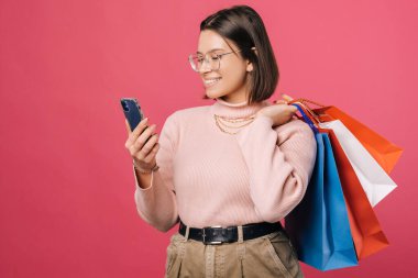 Gözlüklü genç bir kız telefonda sipariş verirken omzunda alışveriş torbaları tutuyor..