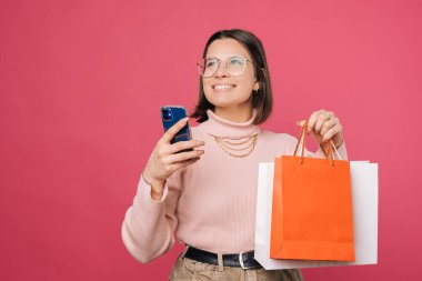 Genç, kısa saçlı kız elinde alışveriş çantaları ve akıllı bir telefon tutuyor..