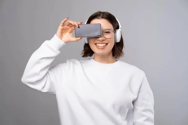 웃고 있는 젊은 여성 이 전화기로 한쪽 눈을 가리고 있습니다. 화면에 복사 공간. — 스톡 사진