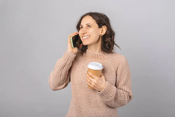 Een glimlachende vrouw heeft een telefoontje terwijl ze een papieren beker vasthoudt.. — Stockfoto