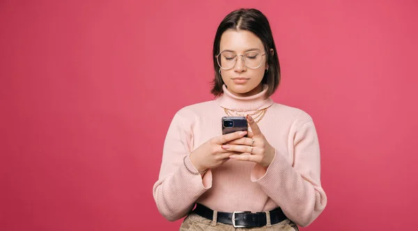 Jovem sério está enviando mensagens de texto no telefone sobre fundo rosa. — Fotografia de Stock
