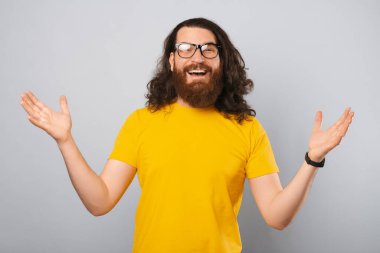 Gözlük takan uzun saçlı sakallı adam kolları açık kalıyor. Stüdyo çekimi açık gri arkaplan üzerine.