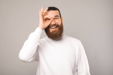 Neşeli sakallı adam, stüdyodaki gri arkaplan üzerinden iyi bir jest yapıyor..