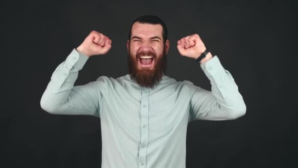Bilder av förbluffad ung skäggig man firar seger med armarna upp — Stockvideo