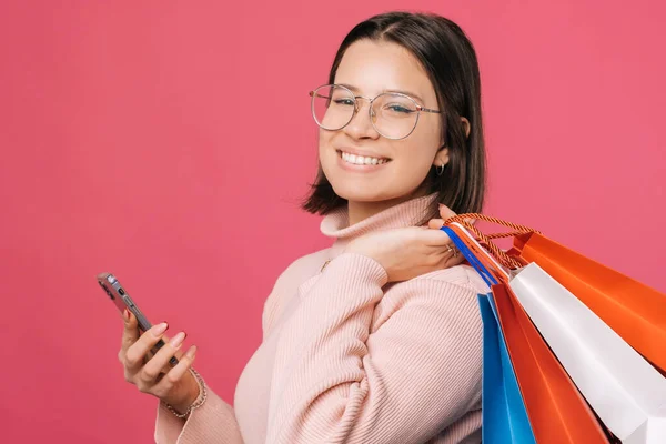 Uśmiechnięta Kobieta Trzyma Ramieniu Torby Zakupy Telefon Różowym Tle — Zdjęcie stockowe