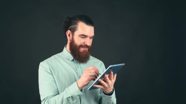 Zamknij film młodego człowieka z brodą w niebieskiej koszuli pracującego na tablecie z długopisem — Wideo stockowe