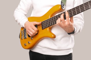 Beyaz giyen, gitar çalan ve pratik yapan bir adamın suratsız fotoğrafı. Stüdyo resmi gri arka planda..