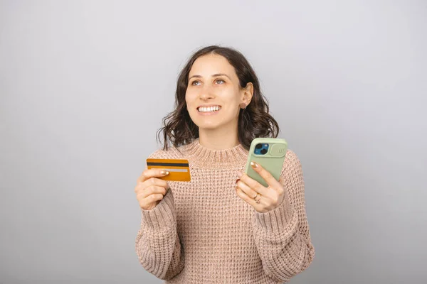 Jonge Glimlachende Vrouw Houdt Een Creditcard Telefoon Een Studio Grijze — Stockfoto