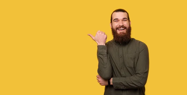 大胡子男子的全景肖像 身穿绿色衬衫 大拇指指向黄色背景 — 图库照片