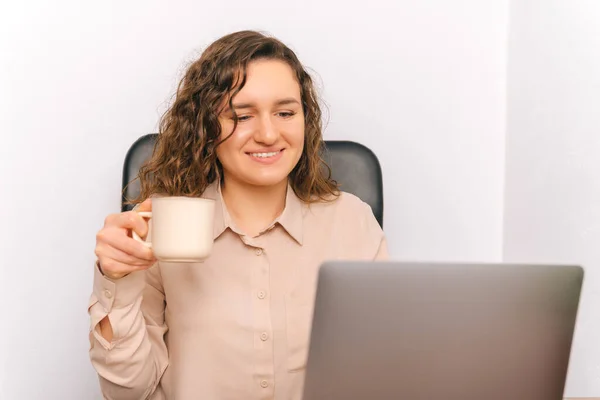 Mujer Joven Sonriente Está Sosteniendo Una Taza Mientras Mira Computadora — Foto de Stock
