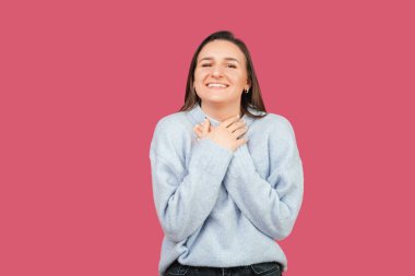 Pembe arka planda gülümseyen heyecanlı ve kendinden geçmiş genç bir kadının portresi. Stüdyo çekimi.