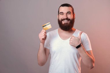 Sakallı, sarı bankamatik kartı tutan ve el hareketi yapan mutlu genç adam..