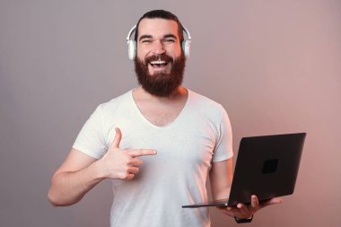 Kulaklık takıp dizüstü bilgisayarı işaret eden heyecanlı genç sakallı adam..