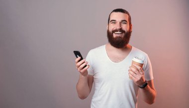 Gülümseyen, sakallı, elinde kahve fincanı olan genç bir adam..