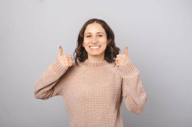 Genç bayan, gri arka planda kameraya gülümserken iki parmağını kaldırıyor..