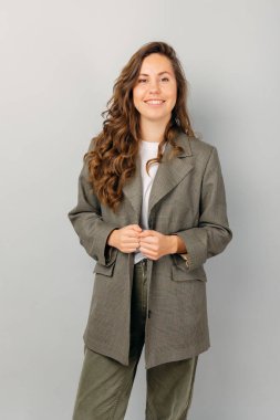 Moda ceket giyen, gülümseyen genç bir kadının dikey portresi. Stüdyo çekimi gri arkaplan üzerinde.