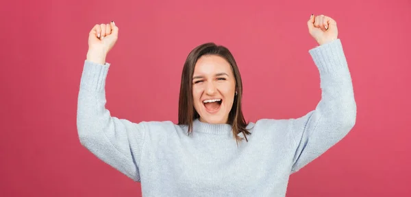 悲鳴を上げながらパノラマの若い勝者の女性が腕を上げてジェスチャーしている スタジオショットオーバーピンクの背景 — ストック写真