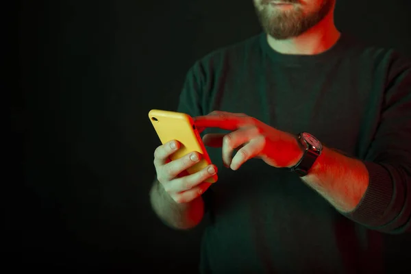 Crop photo d'un homme barbu à l'aide d'un téléphone jaune sur fond sombre. — Photo