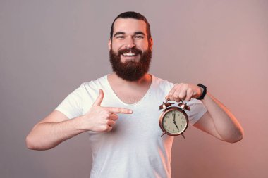 Neşeli sakallı adam elindeki çalar saati işaret ediyor..