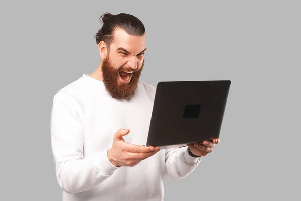 Hipster mâle barbu tient un ordinateur portable ouvert et crier à elle. — Photo