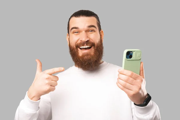 Ecstatic amazed bearded man is holding phone while pointing at it. Stock Photo