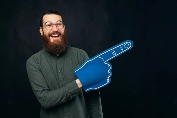 Vzrušený vousatý muž ukazuje stranou s modrou pěnovou rukavicí. — Stock fotografie