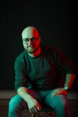 Siyah arka planda kırmızı ve yeşil ışıklı, gözlüklü, patenci sakallı bir adamın dikey portresi..