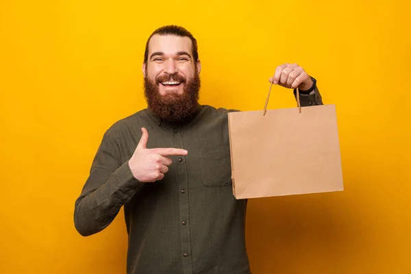 英俊的留着胡子的男人拿着一个带有复制空间的购物袋 指着它 工作室拍摄 — 图库照片