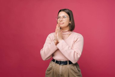 Minnettar genç bayan dua etmek için el ele tutuşuyor. Stüdyo çekimi pembe arkaplanda.