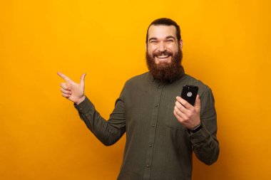 Mest olmuş sakallı adam telefonu elinde tutarken kenara çekiyor. Stüdyo çekimi sarı arkaplanda.