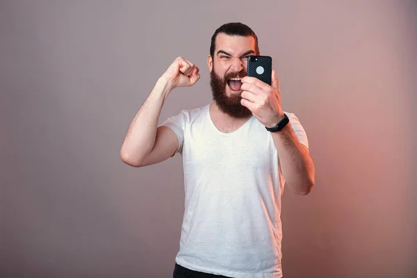 Сильный Бородатый Мужчина Делает Победный Жест Держа Руках Телефон Студийное — стоковое фото