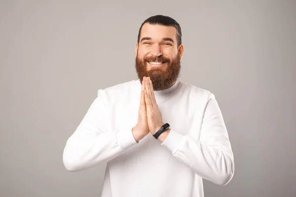 Cute smiling young bearded man is holding hands together for prayer. — Stockfoto