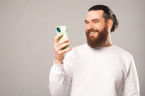 Unga leende skäggig hipster man håller och använder sin smartphone. — Stockfoto