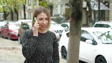 Keyifli genç bir kadın sokakta yürüyor ve akıllı telefondan konuşuyor.