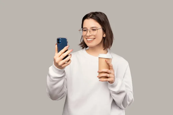 Donna felice sta messaggiando al telefono mentre tiene una tazza di caffè da asporto. — Foto Stock